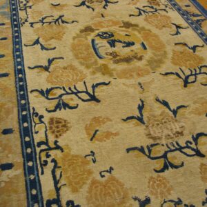 Tan rug with bold navy blue and golden floral patterns, centered motifs, and striped blue borders on wood.