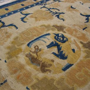 Close-up of a rug with cream ground, blue border, and yellow, gold, brown, and blue traditional patterns.