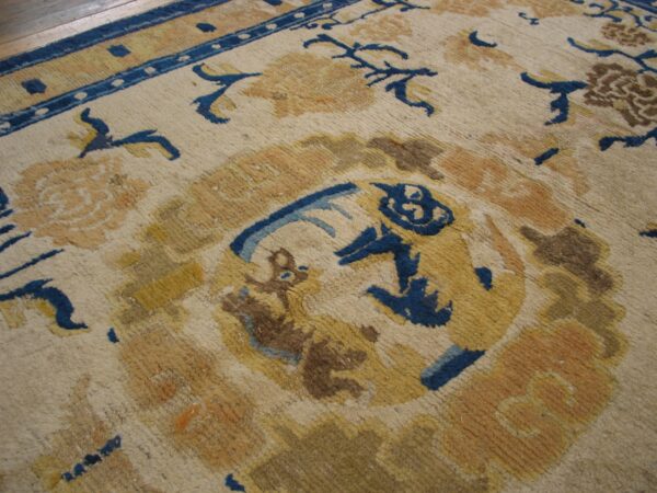 Close-up of a rug with cream ground, blue border, and yellow, gold, brown, and blue traditional patterns.