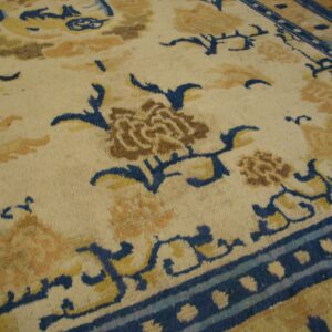 Ivory rug with scrolling blue vines, tan flowers, and brown accents rests on a hardwood floor.