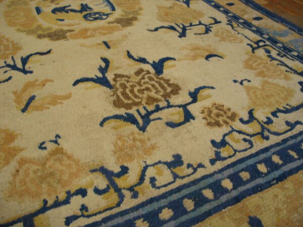 Ivory rug with scrolling blue vines, tan flowers, and brown accents rests on a hardwood floor.