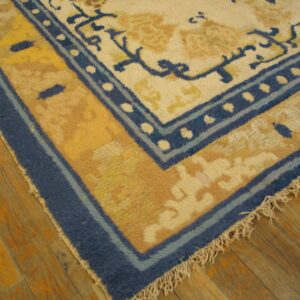Cream rug corner with blue and gold decorative borders rests on shiny warm wood flooring.