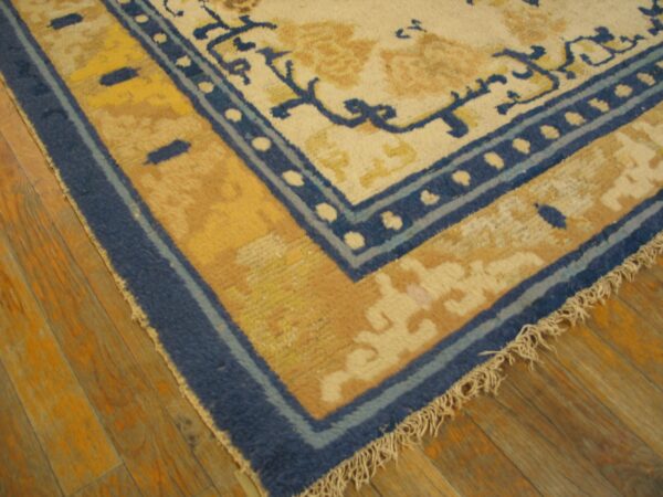 Cream rug corner with blue and gold decorative borders rests on shiny warm wood flooring.