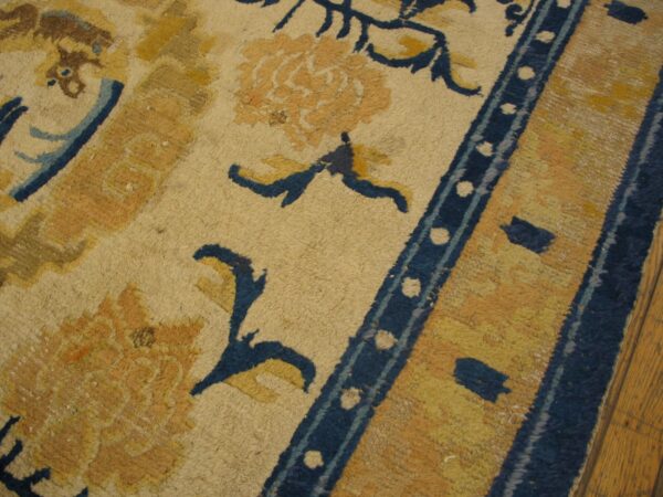 Detailed view of a low-pile rug featuring gold floral designs and navy blue accents on wood flooring.