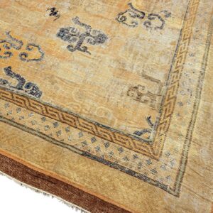 Faded gold and tan rug corner with scattered blue cloud patterns and a detailed geometric brown border.