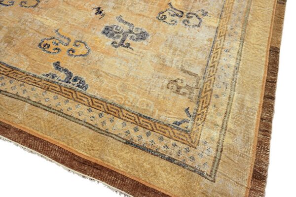 Faded gold and tan rug corner with scattered blue cloud patterns and a detailed geometric brown border.