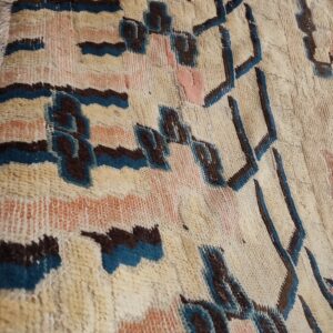 Close-up of a high-pile rug featuring a geometric pattern in cream, dark brown, teal, and peach.