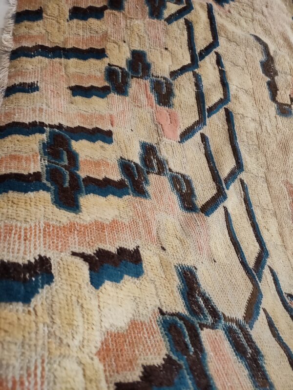 Close-up of a high-pile rug featuring a geometric pattern in cream, dark brown, teal, and peach.