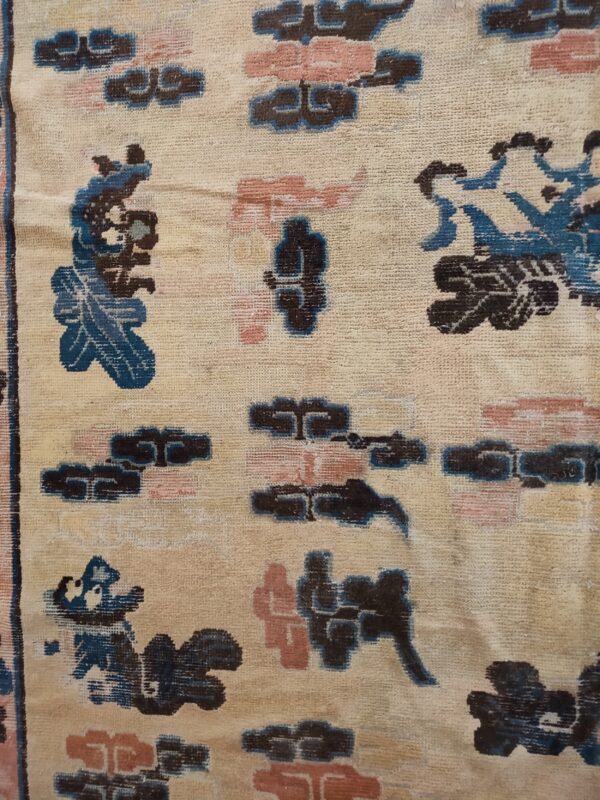 Low-pile rug detail featuring a beige background and scattered, stylized motifs in navy, pink, and teal blue.