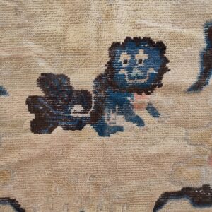 Textured beige high-pile rug detail showing stylized dark blue and brown figures against a light background.
