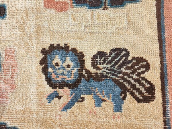 Textured rug close-up with a blue and brown winged creature pattern on a tan background.