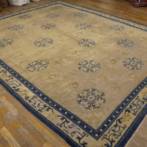 Light gold rug with scattered blue medallions and an elaborate blue border on wood planks.