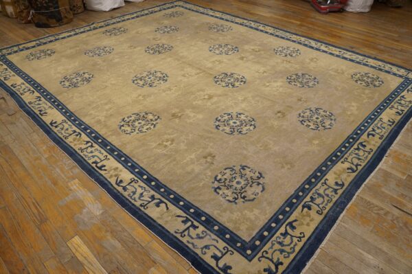 Light gold rug with scattered blue medallions and an elaborate blue border on wood planks.