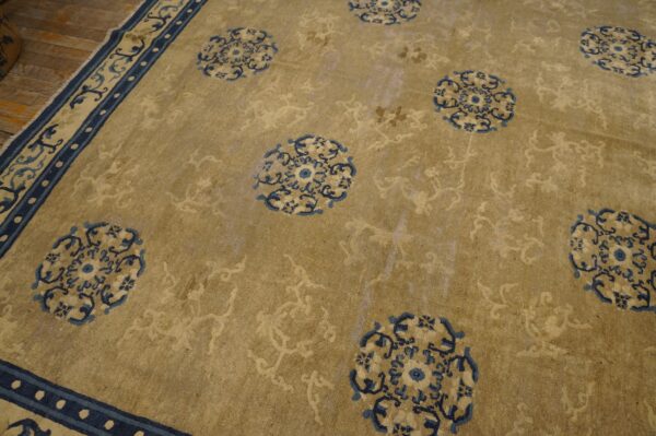 Khaki rug with scattered blue medallions and a detailed navy border rests on wood flooring.