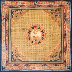 Square tan rug with a central white bird medallion, surrounded by complex blue and red geometric borders.