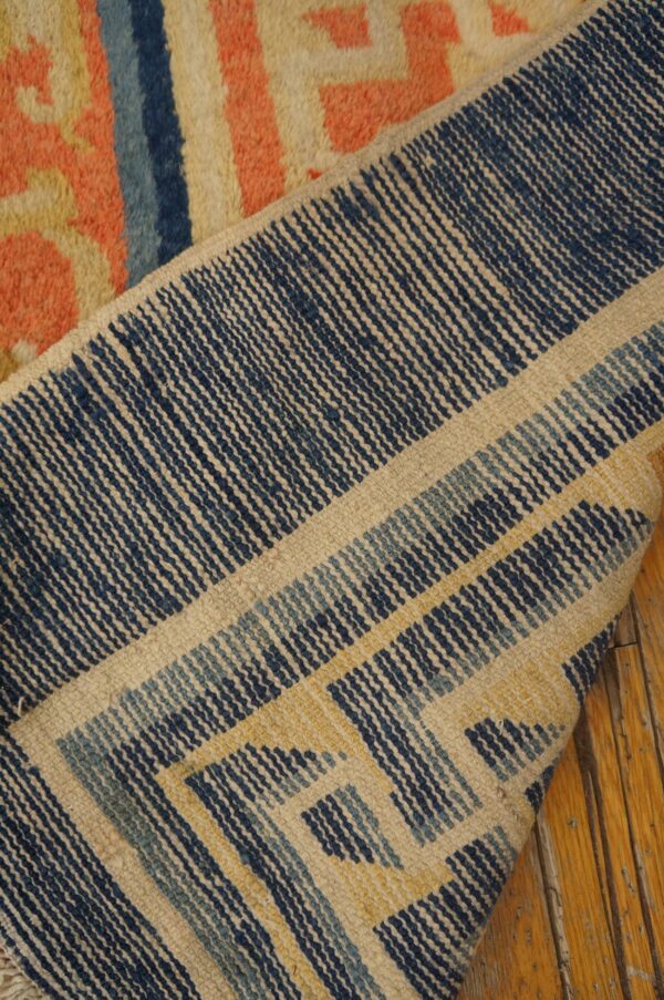 A folded rug displays a textured coral front and a tightly woven navy and cream geometric back.