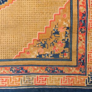 Detailed view of a rug corner with a gold lattice field, blue and red stepped design, and geometric borders.