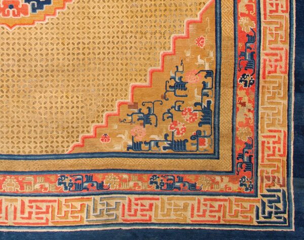 Detailed view of a rug corner with a gold lattice field, blue and red stepped design, and geometric borders.