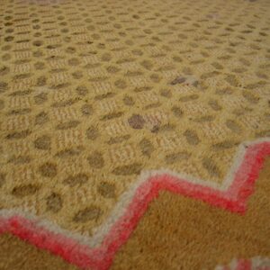 Gold and brown textured rug with repeating dotted patterns and a prominent red zigzag border detail.