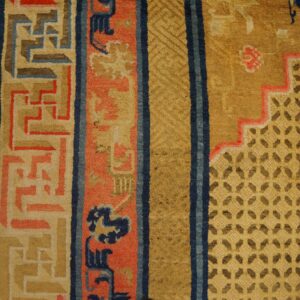 Detail of a yellow and blue rug showing stepped geometric patterns and thick coral borders next to wood floor.