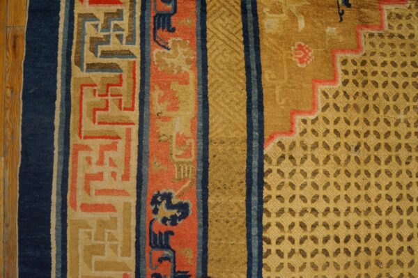 Detail of a yellow and blue rug showing stepped geometric patterns and thick coral borders next to wood floor.