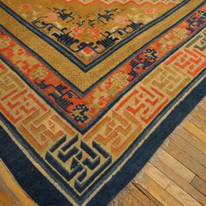 Gold, blue, and coral patterned rug corner on distressed wood flooring.