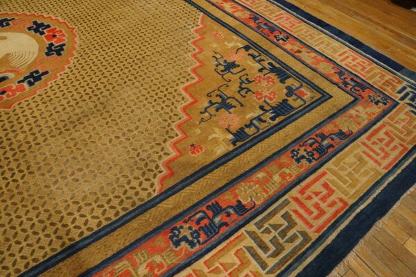 Golden patterned rug with navy blue and coral borders, featuring a partial white bird motif on hardwood floor.