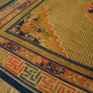 Intricate gold, coral, and navy rug displaying complex borders and a lattice field on wood planks.