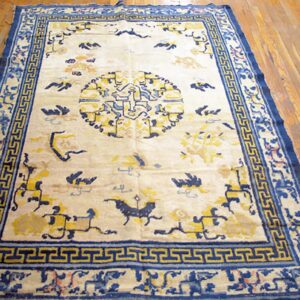 Cream and blue rug featuring a central medallion and T-fret border sits on light brown wood planks.