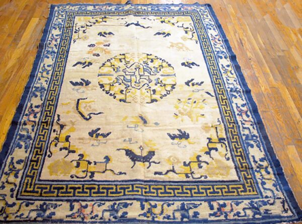 Cream and blue rug featuring a central medallion and t-fret border sits on light brown wood planks.