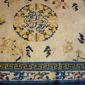 Cream rug detail with a large blue and yellow central medallion and geometric border design.
