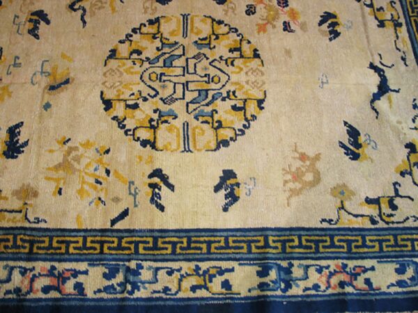 Cream rug detail with a large blue and yellow central medallion and geometric border design.