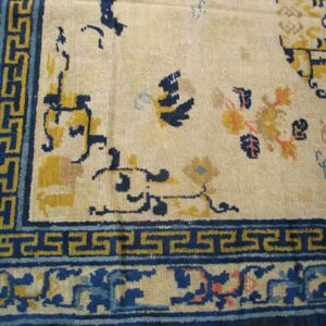 Cream rug featuring dark blue and yellow borders with a prominent Greek key design near the corner.