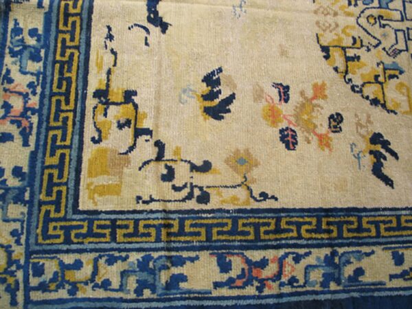 Cream rug featuring dark blue and yellow borders with a prominent greek key design near the corner.