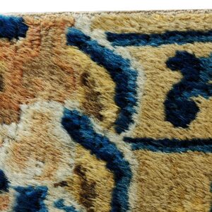 Close detail of a high-pile rug featuring blue abstract shapes contrasting with tan and rust fibers.