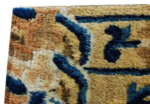 Close detail of a high-pile rug featuring blue abstract shapes contrasting with tan and rust fibers.