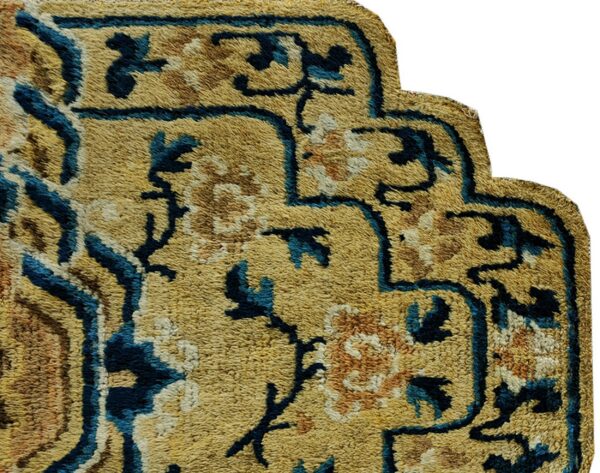 Textured, scalloped rug corner features gold pile with blue and brown traditional floral designs.