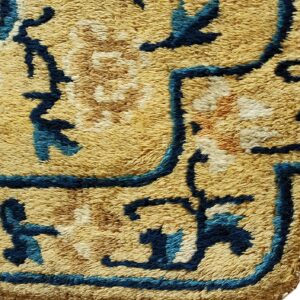 Shaggy rug close-up showing a high pile texture and abstract pattern in gold, blue, and brown.