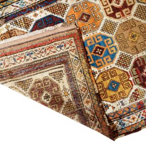 Folded rug displaying a geometric repeating pattern in blue, gold, brown, and cream tones.