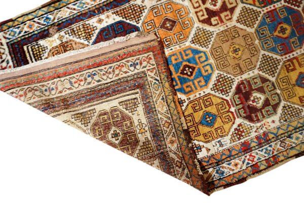 Folded rug displaying a geometric repeating pattern in blue, gold, brown, and cream tones.