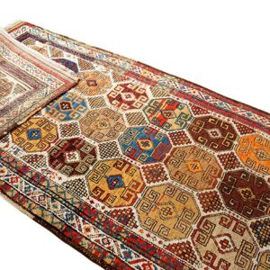 Multi-colored geometric runner rug featuring repeating hexagonal medallions in gold, brown, blue, and red, partially folded.