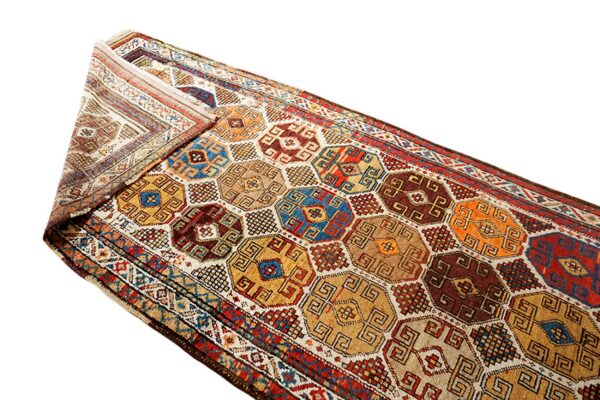 Multi-colored geometric runner rug featuring repeating hexagonal medallions in gold, brown, blue, and red, partially folded.