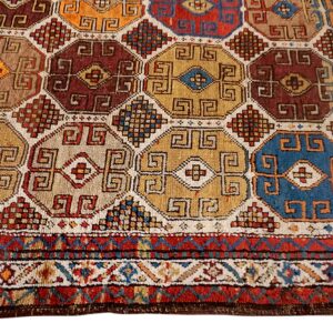 Geometric rug detail with interlocking octagons in red, gold, blue, and maroon colors, featuring a striped border.