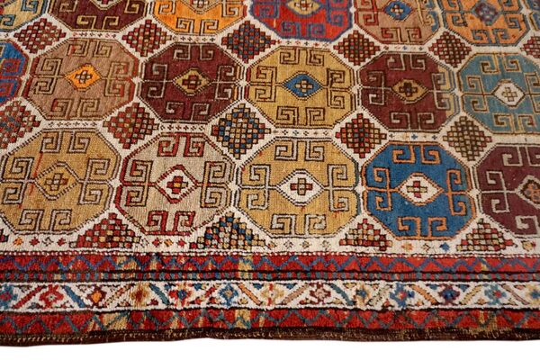 Geometric rug detail with interlocking octagons in red, gold, blue, and maroon colors, featuring a striped border.