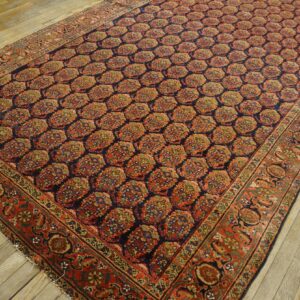 Ornate navy and rust rug featuring a repeating medallion pattern is displayed on rustic wood floorboards.