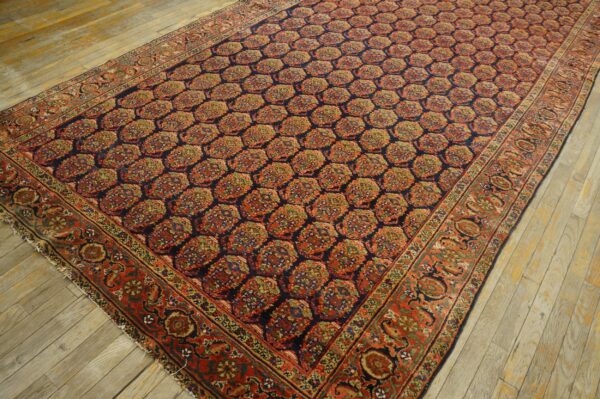Ornate navy and rust rug featuring a repeating medallion pattern is displayed on rustic wood floorboards.