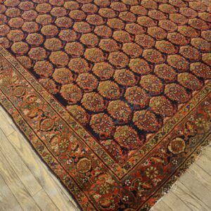 Detailed navy rug with repeating rust-and-green medallions and a broad ornate border on plank wood.