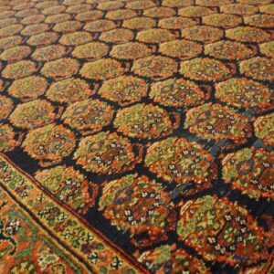 Dark blue rug with repeating rust and green traditional motifs, framed by a multi-layered ornamental border.
