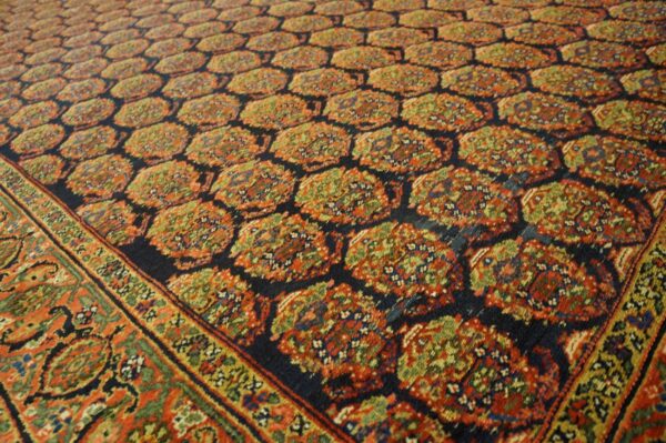 Dark blue rug with repeating rust and green traditional motifs, framed by a multi-layered ornamental border.