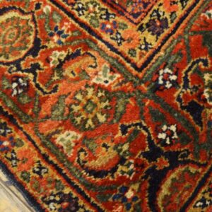 Ornate red, navy, and green traditional rug with high pile resting on distressed light wood floor.